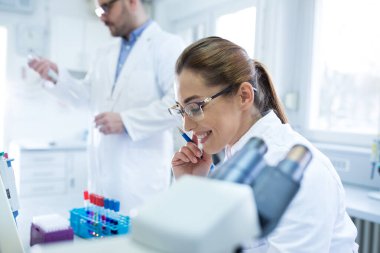 Laboratuvarda test tüpü ve mikroskopla çalışan iki biyolog.