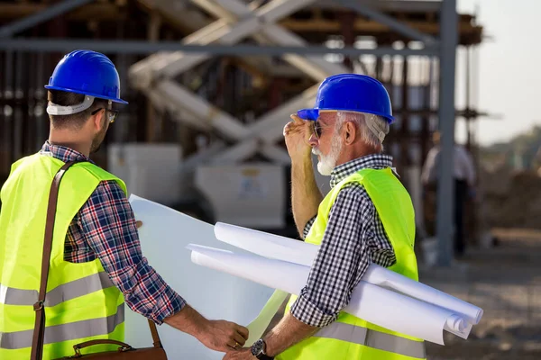 Два Опытных Инженера Рассматривают Чертежи Беседуют Строительной Площадке Металлоконструкцией Заднем — стоковое фото