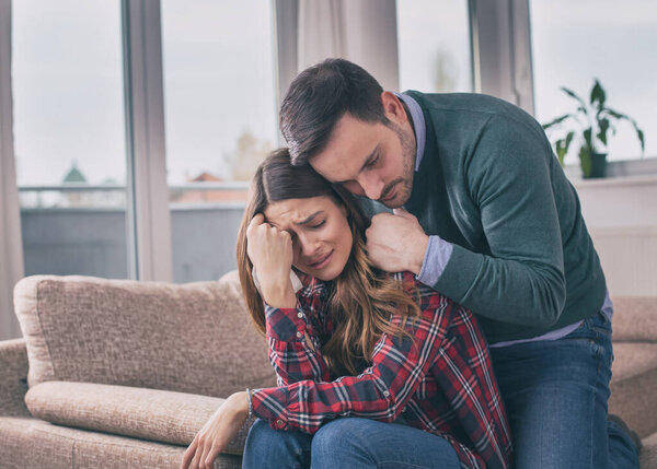 Man consoling sad girl at home with hug and his presence