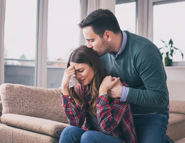 Man consoling sad girl at home with hug, kiss and his presence