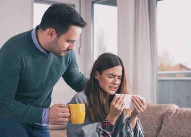 Erkek arkadaşı çay getiriyor ve grip olan kızla ilgileniyor. Evdeki kanepede battaniye ve hapşırıkla otururken