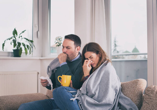 Young couple having virus or flu, covered with blanket sitting on sofa in home isolation during pandemic
