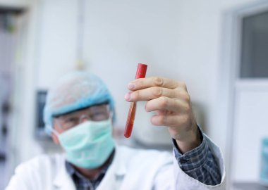 Doktorun elinin üzerinde kan olan test tüpünü tutarken yakın plan. Laboratuvarda salgın testi