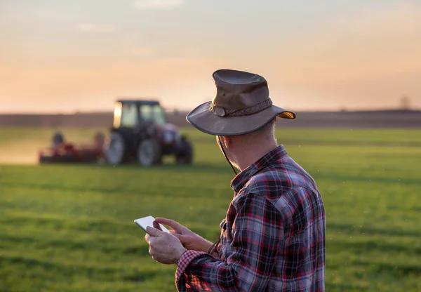 Şapka Tabletini Tarlada Tutan Kıdemli Çiftçi Arka Planda Çalışan Traktöre — Stok fotoğraf