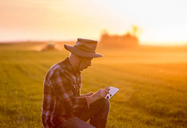 Contadino Accovacciato Sul Campo Guardando Tablet Mentre Trattore Lavora Background — Foto Stock