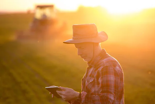 Farmář Dívá Tabletu Poli Před Traktorem Pozadí Při Západu Slunce — Stock fotografie