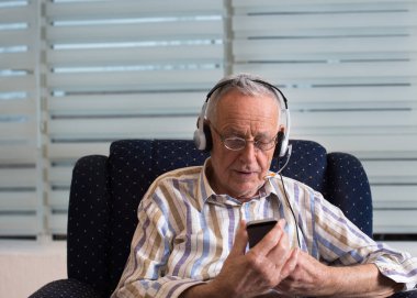 Salgın sırasında sevdikleriyle iletişim kurmak için cep telefonu ve kulaklık tutan kıdemli bir adam.