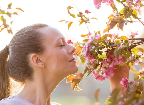 美丽的年轻女子在花园里闻到美丽的粉色花朵树的芬芳 — 图库照片