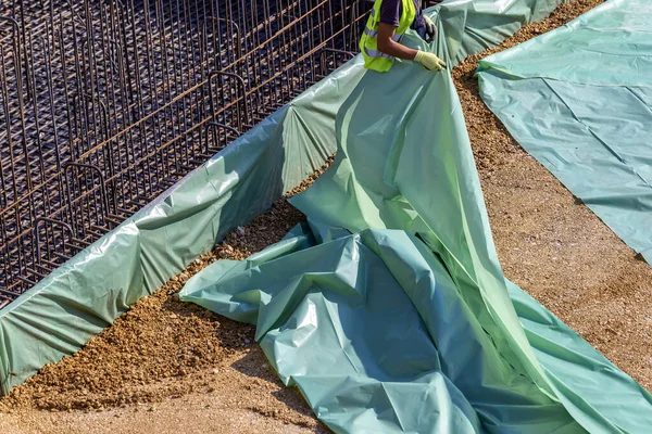 Trabajador instalación de membrana de plástico antes de verter losa de hormigón —  Fotos de Stock