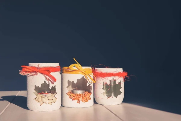 Üç cam kavanoz masanın üzerinde, şamdanla süslenmiş, içinde mum ve bezelye ile akçaağaç yaprağı şeklinde bir pencere. Dikiş işi ve manuel yaratıcılık kavramı..