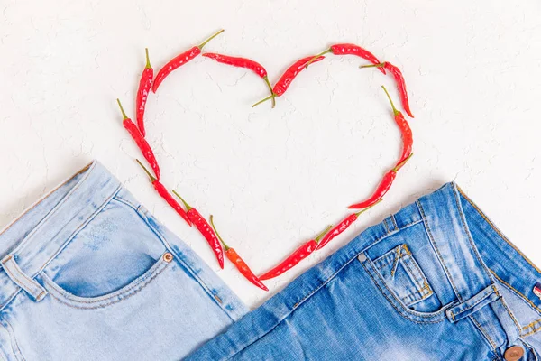 İki çift kot pantolon ve beyaz desenli arka planda kırmızı biberli bir kalp.. Stok Fotoğraf