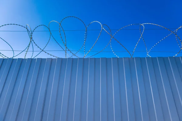 Arame farpado com rolou em uma cerca de piquete contra um céu azul — Fotografia de Stock