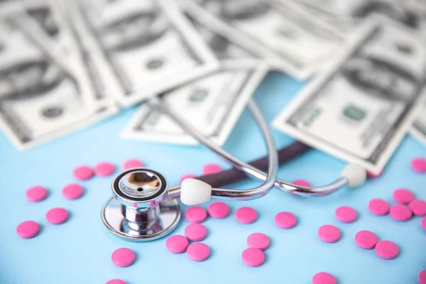 Yansımalı tıbbi steteskop ve renkli pembe haplar. Mavi arka planda hapların kabarcıkları. İlaç, tedavi, beslenme takviyeleri, sağlık, koronavirüs salgını. Seçici odak.
