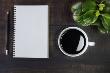 Boş sayfaları olan açık okul defterinin en üst görüntüsü, tahta masa arkasında kalem, bitki ve kahve fincanı. Kopya alanı ile iş, ofis veya eğitim kavramı.