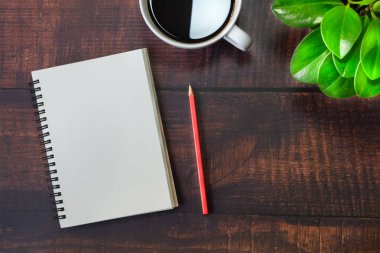 Boş sayfaları olan açık okul defterinin en üst görüntüsü, tahta masa arkasında kalem, bitki ve kahve fincanı. Kopya alanı ile iş, ofis veya eğitim kavramı.