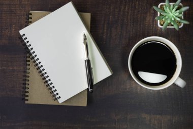 Boş sayfaları olan açık okul defterinin en üst görüntüsü. Ahşap masa arkasında Pen, Bitki ve Kahve Bardağı. Kopya alanı ile iş, ofis veya eğitim kavramı.