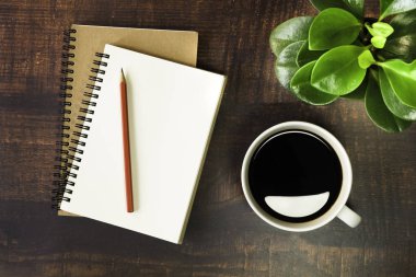 Boş sayfaları olan açık okul defterlerinin en üst görüntüsü, tahta masa arkasında kalem, bitki ve kahve fincanı. Fotokopi alanı ile iş, ofis veya eğitim kavramı. düz yat