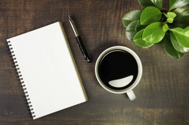 Boş sayfaları olan açık okul defterinin en üst görüntüsü. Ahşap masa arkasında Pen, Bitki ve Kahve Bardağı. Kopya alanı ile iş, ofis veya eğitim kavramı.