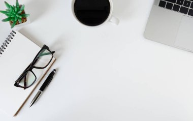 Düz yerde, dizüstü bilgisayarı, defteri, kalemi, siyah kahve fincanı ve gözlüğü olan beyaz ofis masası. Kopyalama alanı olan üst görünüm.