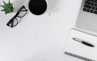 Düz yerde, dizüstü bilgisayarı, defteri, kalemi, siyah kahve fincanı ve gözlüğü olan beyaz ofis masası. Kopyalama alanı olan üst görünüm.
