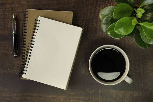 Top view of open school notebook with blank pages, Pen, Plant and Coffee cup on wooden table background. Business, office or education concept with copy space.