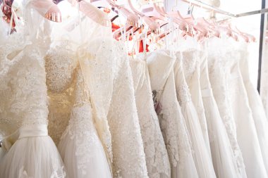 Arka planda güzel, beyaz gelinlik dokusu. Düğün elbiseleri, gelinlik salonunun iç tarafındaki askıda asılı. Tasarım, moda modern lüks detaylarıyla.