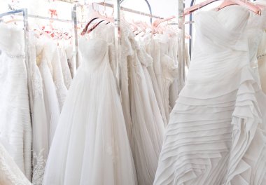 Arka planda güzel, beyaz gelinlik dokusu. Düğün elbiseleri, gelinlik salonunun iç tarafındaki askıda asılı. Tasarım, moda modern lüks detaylarıyla.