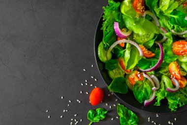 Fresh green vegetable salad. View from above of cherry tomato, onion, spinach and lettuce in black bowl. Healthy concept, home made. Diet vegetable for a tasty and meal. Top view, with copy space.