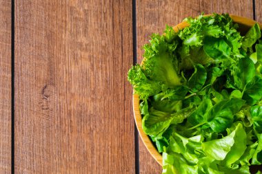 Fresh green vegetable leaves mix. Healthy food salad, Top view from above of spinach, lettuce in wooden bowl on wood table background. Home made, diet vegetable for tasty and meal with copy space.