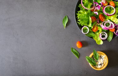 Taze yeşil sebze salatası. Siyah kasede vişneli domates, soğan, ıspanak ve marul. Susamlı salata sosuyla. Ev yapımı, lezzetli ve sağlıklı yemekler için diyet sebze. Üst görünüm, alanı kopyala.