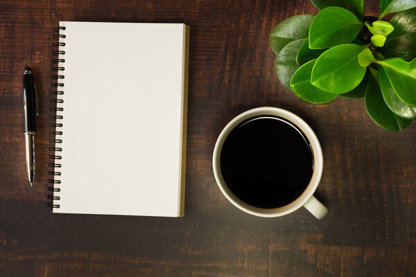 Top view of open school notebook with blank pages, Pen, Plant and Coffee cup on wooden table background. Business, office or education concept with copy space.
