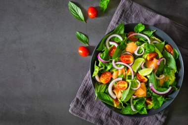Somon salatası, taze domates, soğan, ıspanak, marul, siyah kasede fesleğen, siyah peçeteli sırt üstü. Sağlıklı yemek, ev yapımı konsept. Lezzetli ve lezzetli. Üst görünüm, alanı kopyala.