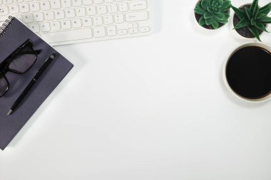 Çalışma alanı, beyaz ofis masası. Klavye, kalem, defterler, gözlükler, saksı, sulu bitkiler, bir fincan sade kahve. Üst manzara, fotokopi alanı olan düz bir yer. İş konsepti.