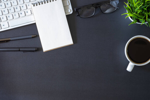 Workplace office with dark black desk. Top view from above of keyboard with notepad and coffee cup. Space for modern creative work of designer. Flat lay with copy space. Business and  finance concept.