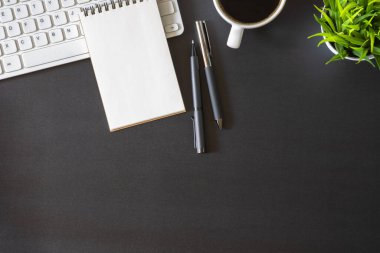 Koyu siyah masalı işyeri ofisi. Üzerinde not defteri ve kahve fincanı olan klavyenin üst görüntüsü. Modern yaratıcı tasarımcılar için yer var. Fotokopi alanı olan düz bir yer. İş ve finans kavramı.