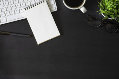 Koyu siyah masalı işyeri ofisi. Üzerinde not defteri ve kahve fincanı olan klavyenin üst görüntüsü. Modern yaratıcı tasarımcılar için yer var. Fotokopi alanı olan düz bir yer. İş ve finans kavramı.