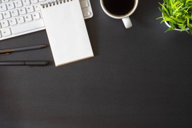 Koyu siyah masalı işyeri ofisi. Üzerinde not defteri ve kahve fincanı olan klavyenin üst görüntüsü. Modern yaratıcı tasarımcılar için yer var. Fotokopi alanı olan düz bir yer. İş ve finans kavramı.