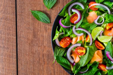 Taze domates, soğan, ıspanak, marul ve fesleğen ile ahşap arka planda duran somon salatasının üst görüntüsü. Ev yapımı konsept. Lezzetli ve sağlıklı sebzeler. Kopyalama alanı olan düz.