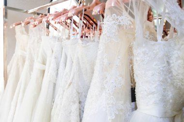Arka planda güzel, beyaz gelinlik dokusu. Düğün elbiseleri, gelinlik salonunun iç tarafındaki askıda asılı. Tasarım, moda modern lüks detaylarıyla.