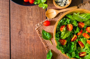 Kırmızı kiraz domatesli taze yeşil sebze, soğan ve marullu ıspanak. Tahta kasede salata susamı sosu. Lezzetli ve sağlıklı yemekler için diyet menüsü. Düz, kopyalama alanı ile.