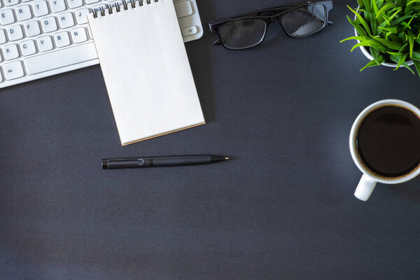 Workplace office with dark black desk. Top view from above of keyboard with notepad and coffee cup. Space for modern creative work of designer. Flat lay with copy space. Business and  finance concept.