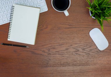 Beyaz ofis masasında yatıyordu. Yukarıdan klavye, bilgisayar faresi, kalem, defterler, gözlükler ve bir fincan sade kahveyle ahşap masaya bakın. Kopyalama alanı olan üst görünüm. İş konsepti.