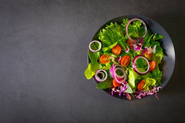 Taze yeşil sebze salatası. Üzerinde soğan, ıspanak ve siyah kasede salatayla birlikte koyu arkaplan olan vişneli domatesin üst görüntüsü. Diyet sebzeler lezzetli ve sağlıklı yemekler. Kopyalama alanı olan düz.