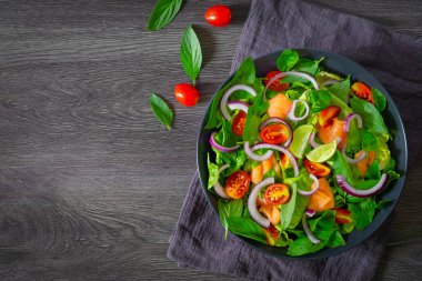 Somon salatası, taze domatesin üst görüntüsü, ıspanaklı soğan, marul ve siyah kasede siyah peçeteli fesleğen. Sağlıklı lezzetli yemekler, ev yapımı konsept. Kopyalama alanı olan düz.