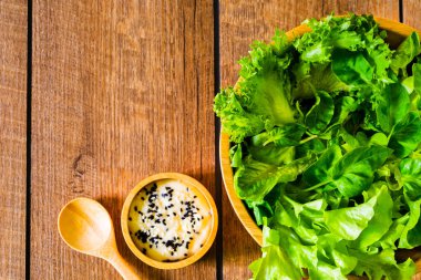 Taze yeşil sebze. Sağlıklı yemek salatası için diyet menüsü ıspanağın yukarıdan görünüşü ahşap masa arkasında marul kasesi. Tahta kasede salata susamı sosu. Kopyalama alanı olan düz.