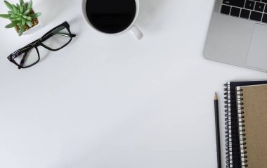 Ofiste beyaz masalı bir iş yeri. Not defteri ve kahveyle dizüstü bilgisayarın üst görüntüsü. Modern yaratıcı tasarımcılar için yer var. Boş fotokopi alanı olan düz bir yer. İş ve finans kavramı.