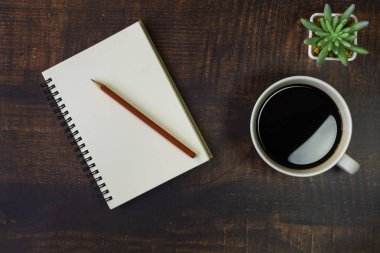Boş sayfaları, kırmızı kalemi, tahta masa arkasında bitki ve kahve fincanı olan açık okul defterinin en üst görüntüsü. Kopya alanı ile iş, ofis veya eğitim kavramı.