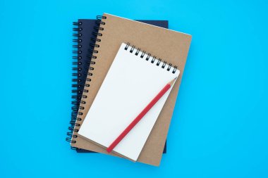 Açılıp kapanan iki spiral defterin üstündeki üst görünüm, açık mavi arka planda izole edilmiş kırmızı kalemle bir model tasarlamak için istiflenmiş. Eğitim ve iş konsepti. düz yat