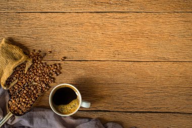 Sabah menüsünde süt köpüğü ve beyaz seramik bardakta kahve çekirdekleri ile ahşap arka planda çuval şeklinde kavrulmuş kahve. Kopyalama alanı olan düz.