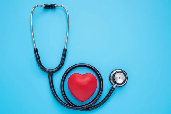 Black stethoscope with red heart of doctor for checkup on blue background. Stethoscope equipment of medical use to diagnose hear sound. Health care and cardiology concept. flat lay with copy space.
